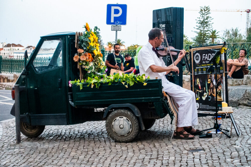 Straßenmusiker sitz auf einem kleinen blumengeschmückten Dreirad-Transporter
